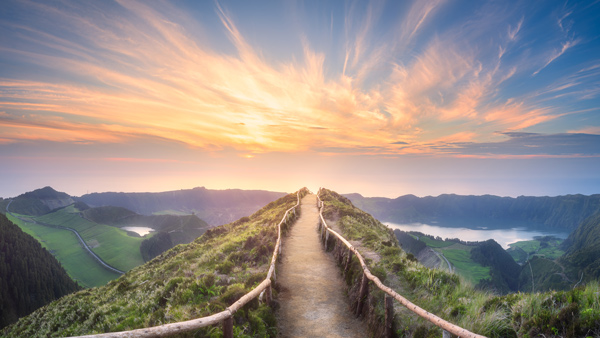 scenic pathway leading to horizon with vibrant sunset over green hills and water showcasing natural beauty and adventure 2 travelers 2 experiences