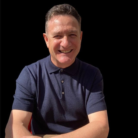 smiling man wearing navy polo shirt against black background sitting outdoors with sunlight highlighting his face enjoying positive moments in life two layers of joy