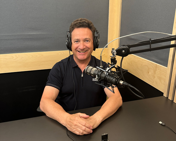 man sitting at a microphone in a recording studio smiling headphones on host and guest setup